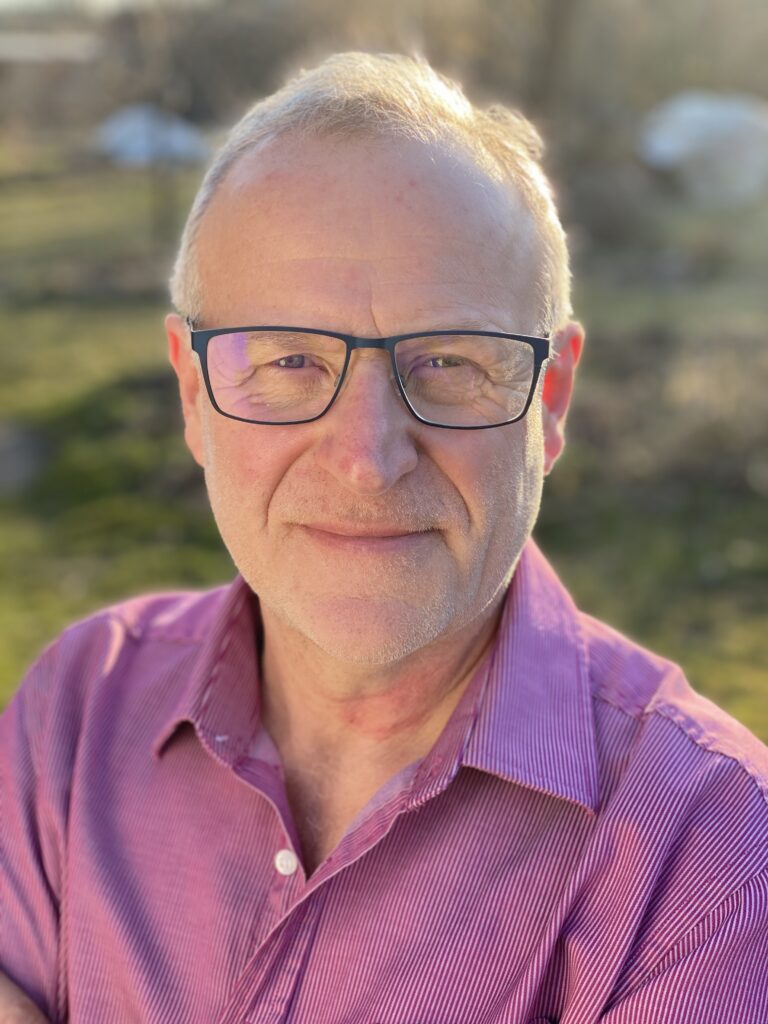 Portrait von Robert Strauch, er stehtim Garten, hat kurze Haare, trägt eine Brille und ein Hemd.