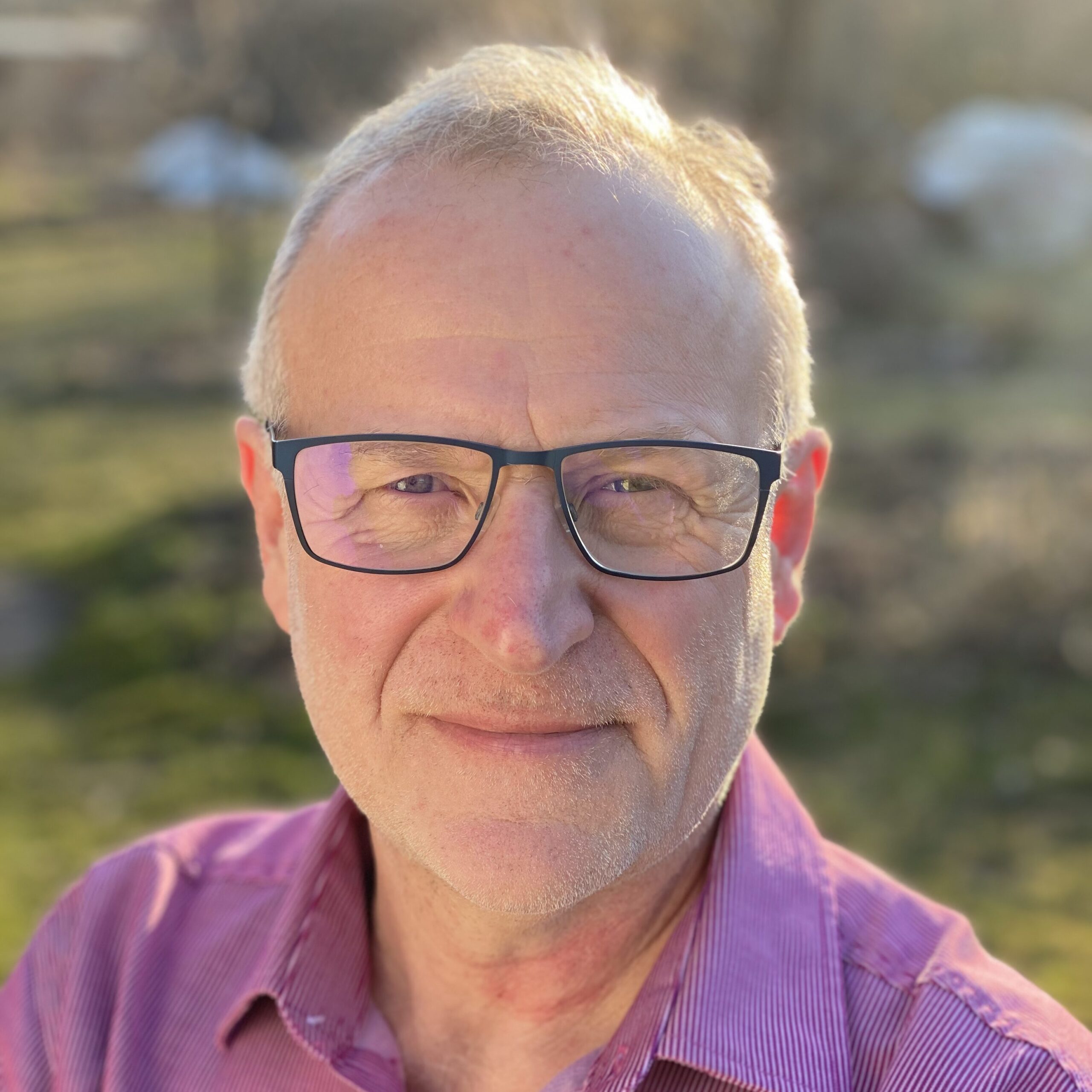 Portrait von Robert Strauch, er stehtim Garten, hat kurze Haare, trägt eine Brille und ein Hemd.